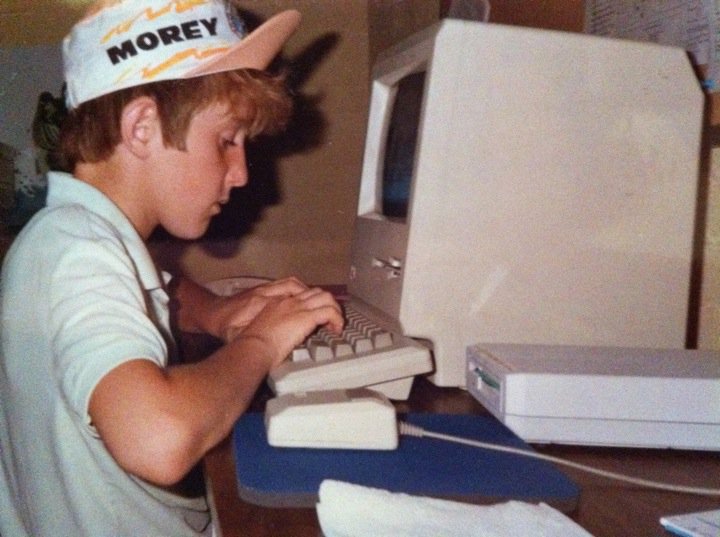 Robert age eight wearing a cloth Morey Boogie cap with upturned peach-coloured brim and pale green polo shirt with upturned collar typing on an original Macintosh computer